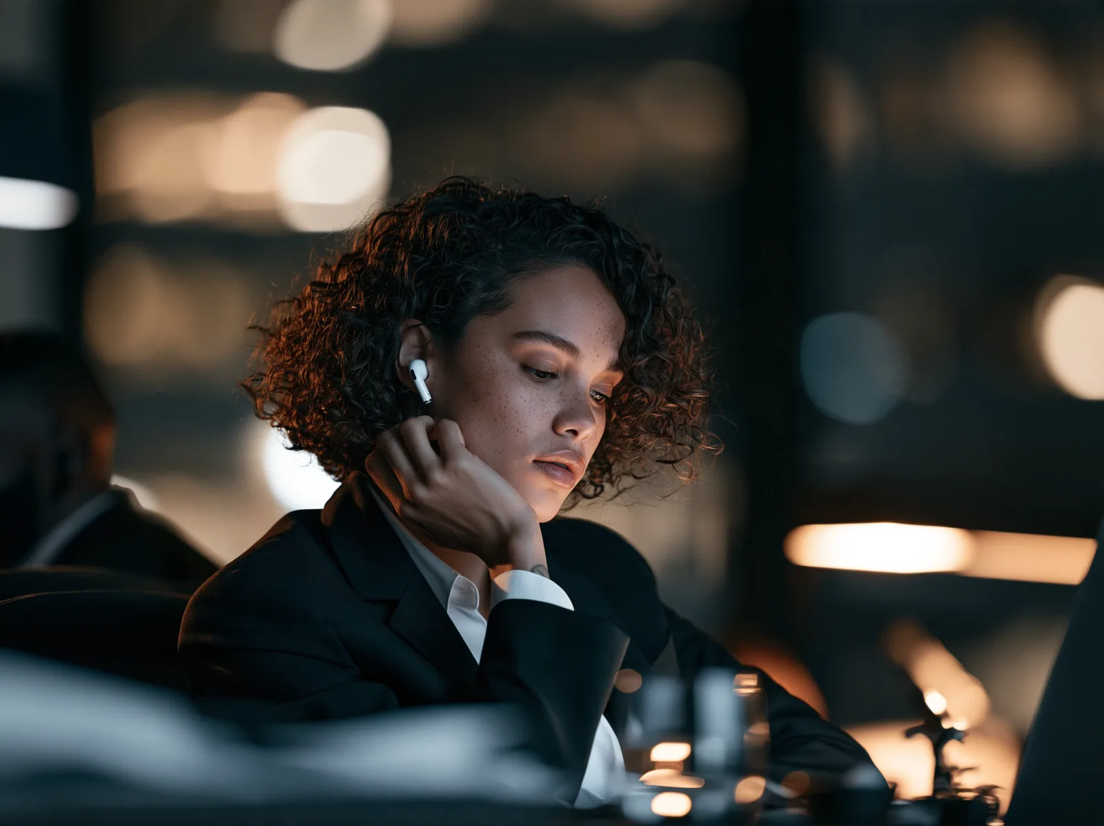 A woman on a call through her earbuds at her desk at night