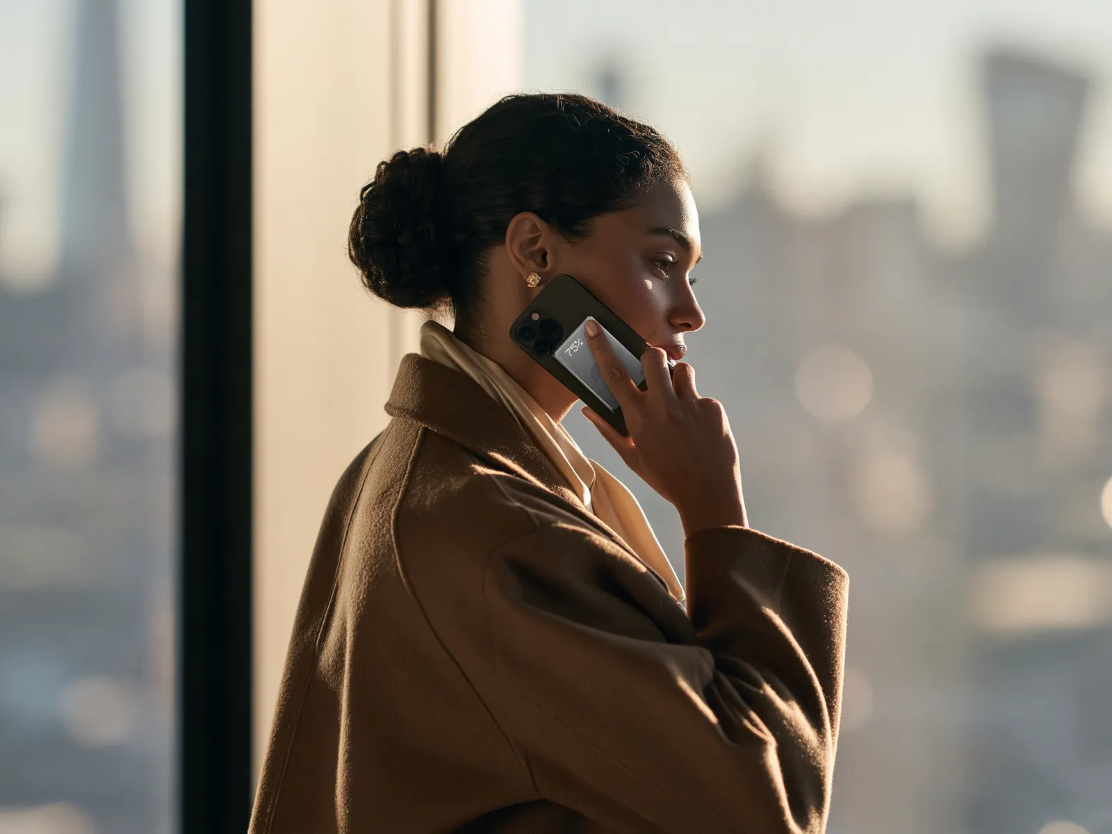 A woman taking a call by a window, Flynn attached to the back of her phone